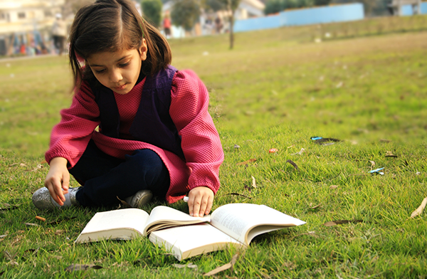 Young girl reading outside on the grass