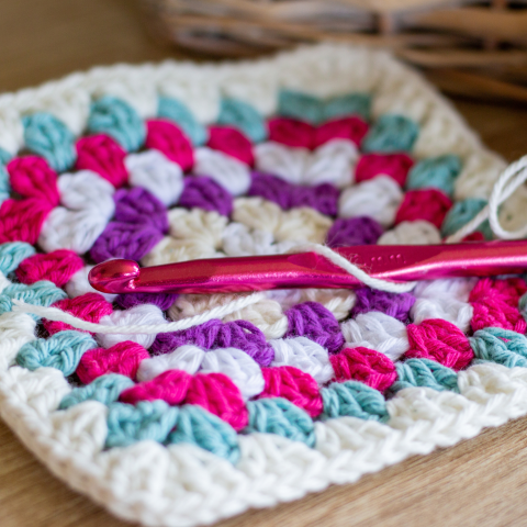 Close up of a crocheted granny square made with white, blue, pink and purple yarn.