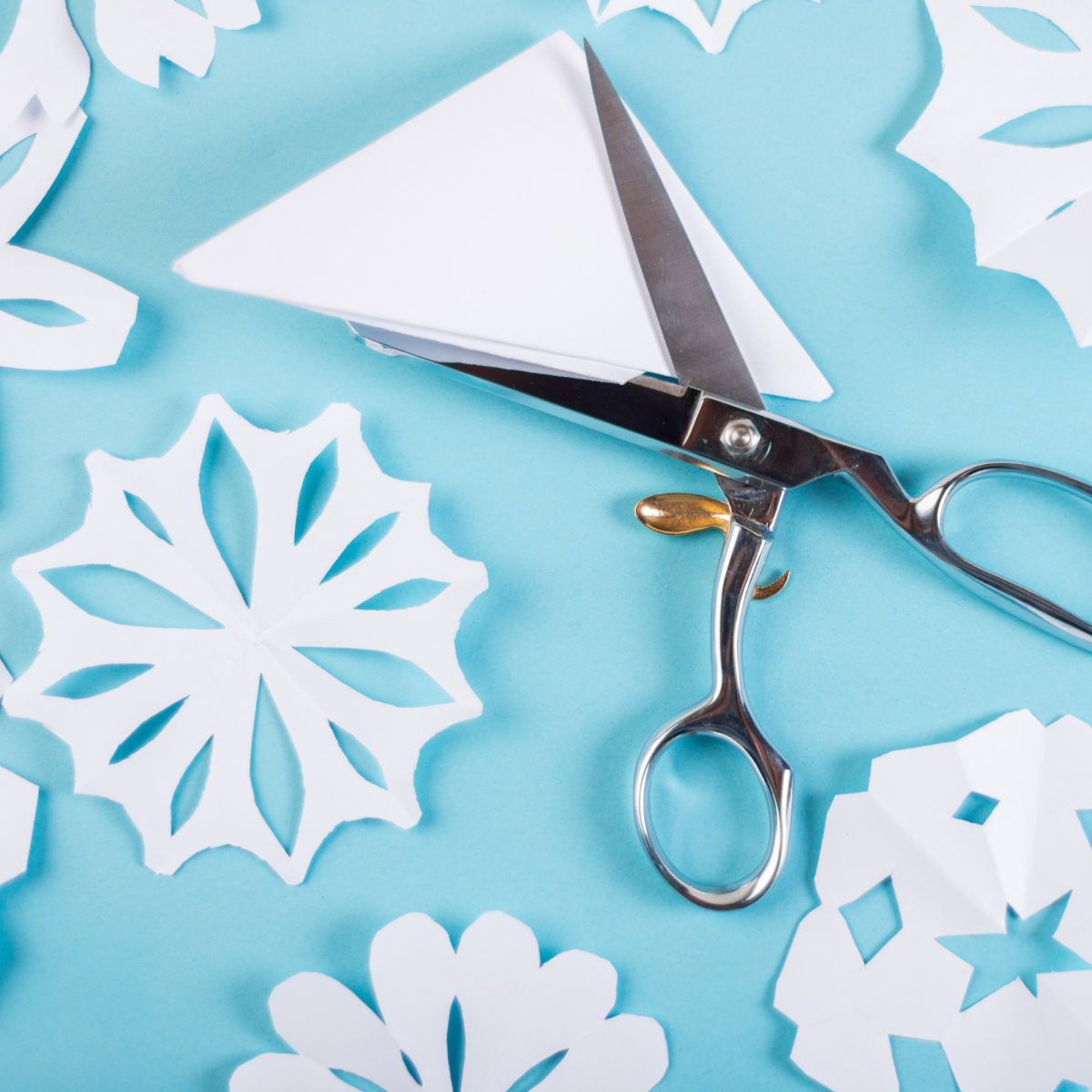 Image of paper snowflakes and a pair of scissors on a blue background